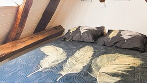 Une chambre mansardée avec des poutres apparentes, un plafond en pente et une couvre-lit bleue à motifs.