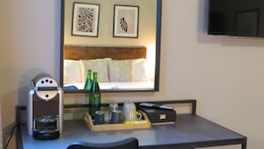 Habitación de hotel con cama, cafetera, bandeja con tazas y botellas, televisor y cesto de basura.