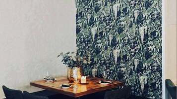 Un comedor con una mesa de madera, sillas negras y una pared con un diseño de hojas.