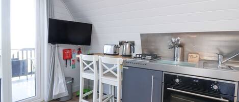 A compact kitchen with a stove, oven, and a flat-screen TV mounted on the wall.