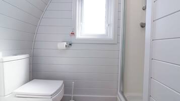 A compact bathroom with a white toilet, a small window, and a toilet brush.