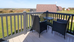 Ein Balkon mit Korbstühlen und einem Tisch, der auf eine ländliche Landschaft mit einem Haus und Feldern blickt.