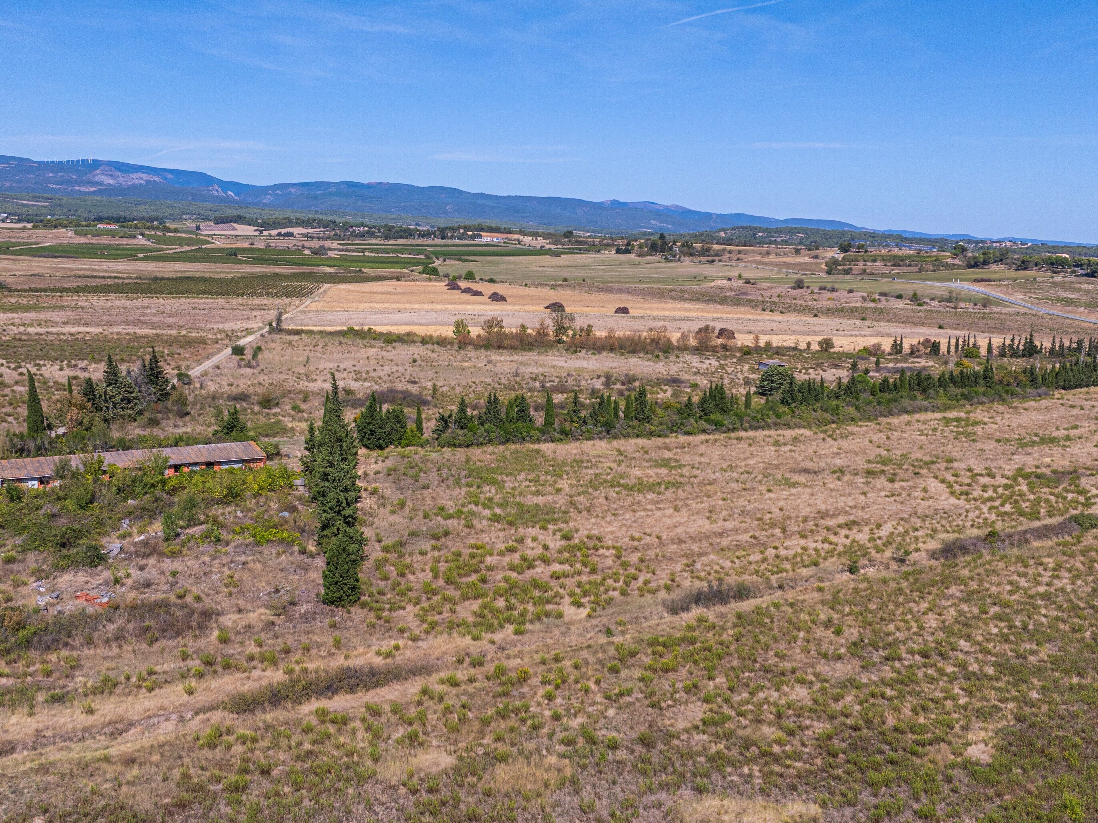 A rural landscape with fields, a few buildings, and distant mountains.