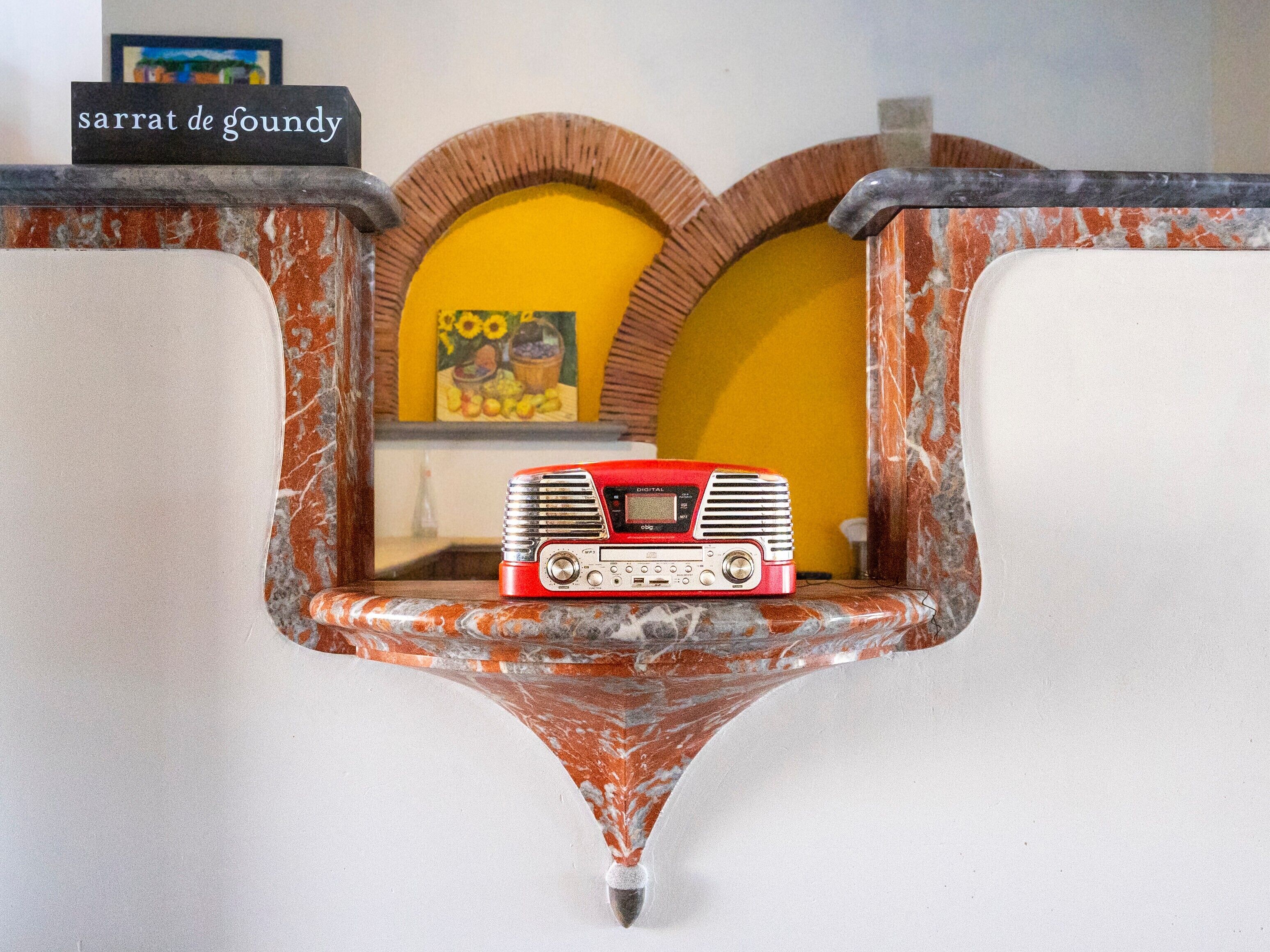 Une radio ancienne posée sur une étagère en marbre, avec un mur jaune et un tableau en arrière-plan.