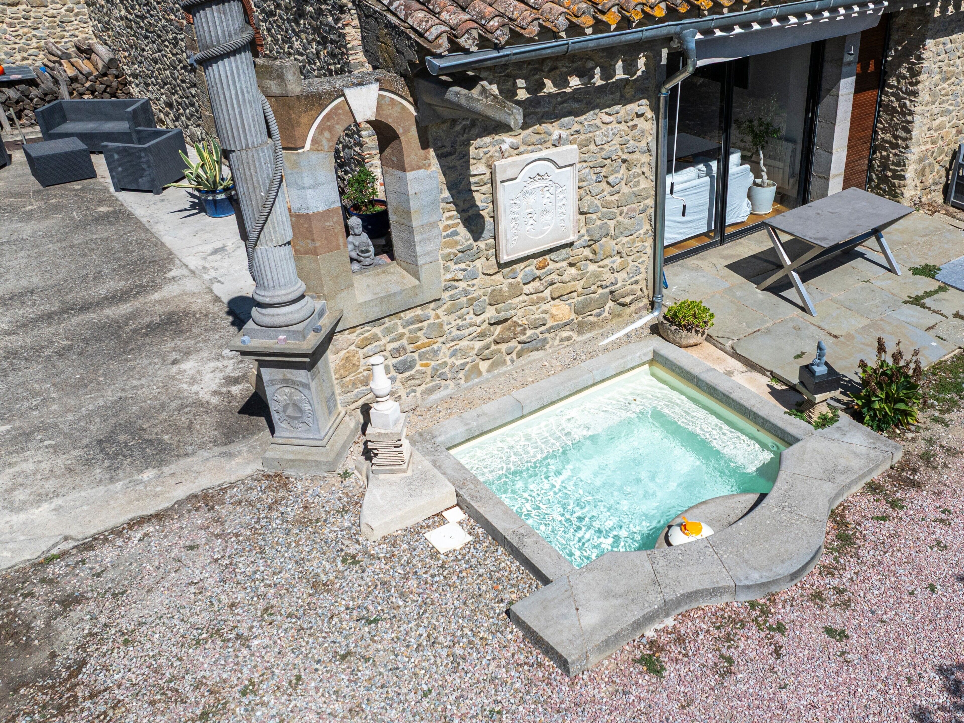 A stone building with a swimming pool, outdoor seating, and a stone wall.