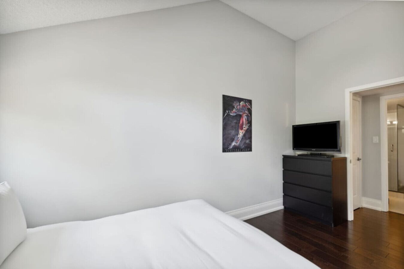 A bedroom with a bed, a dresser, a TV, and a door leading to another room.