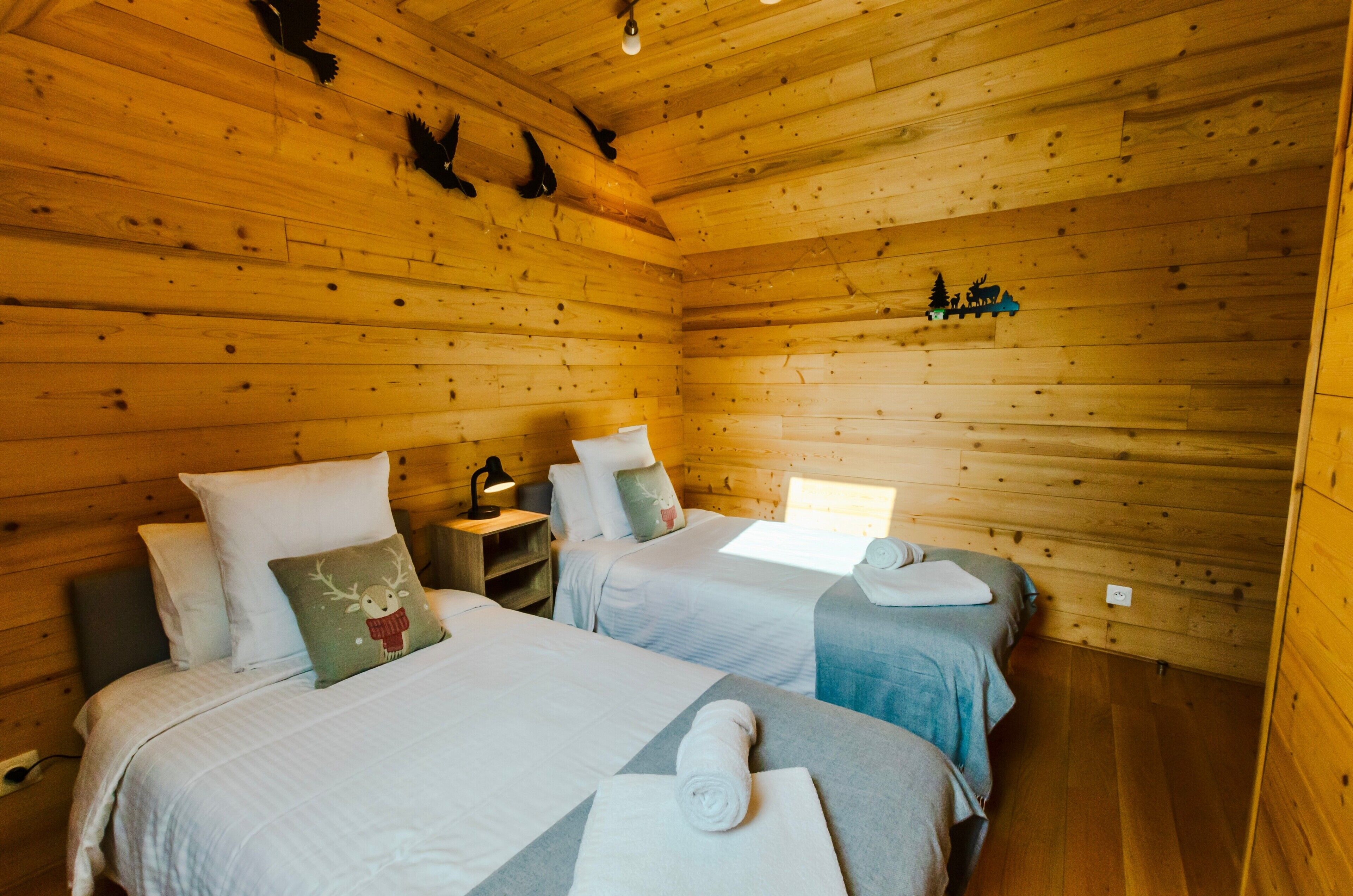 Una habitación tipo cabaña de madera con dos camas, una mesita de noche, una lámpara y un adorno en la pared.