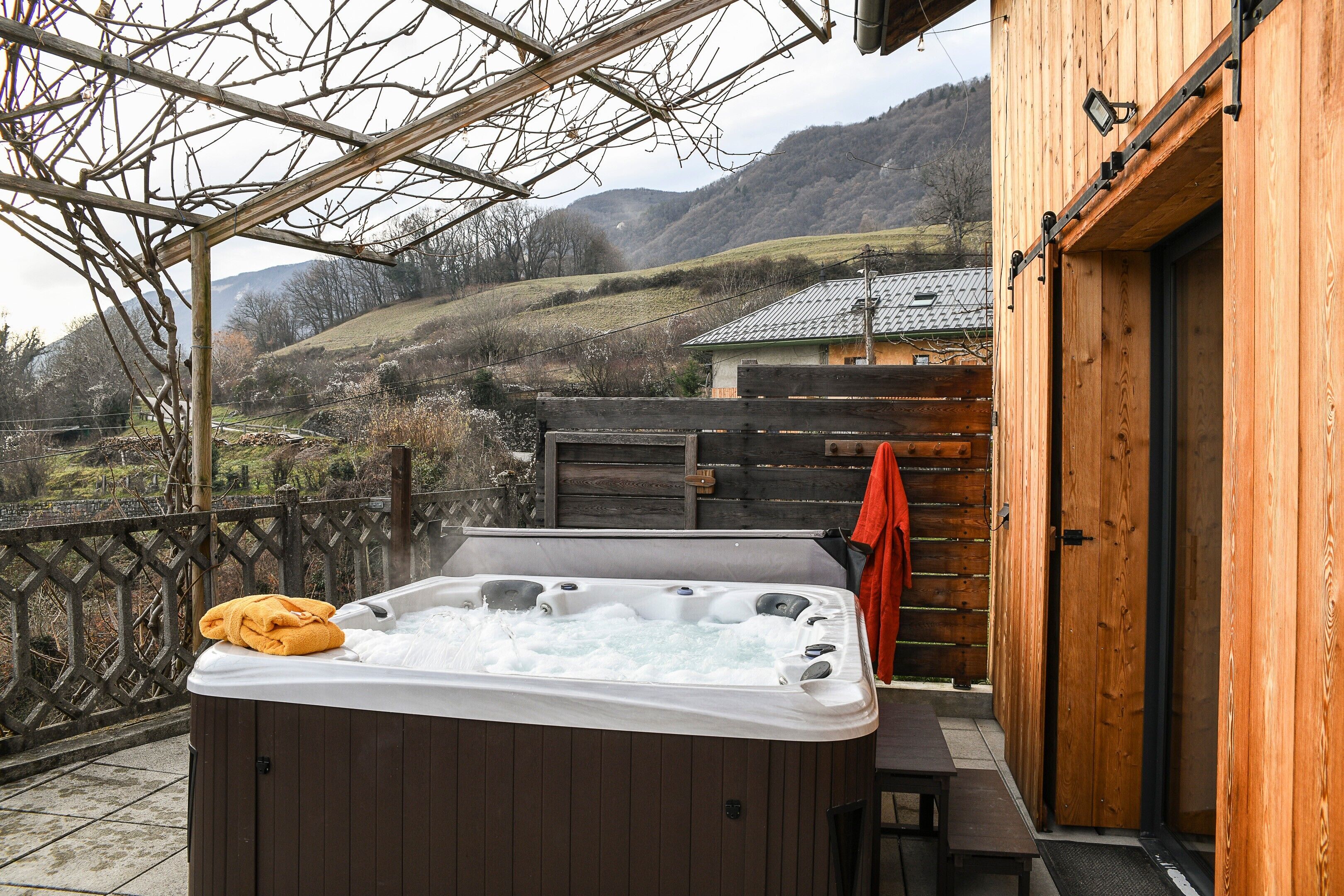 A wooden cabin with a hot tub on a balcony overlooking a mountainous landscape.