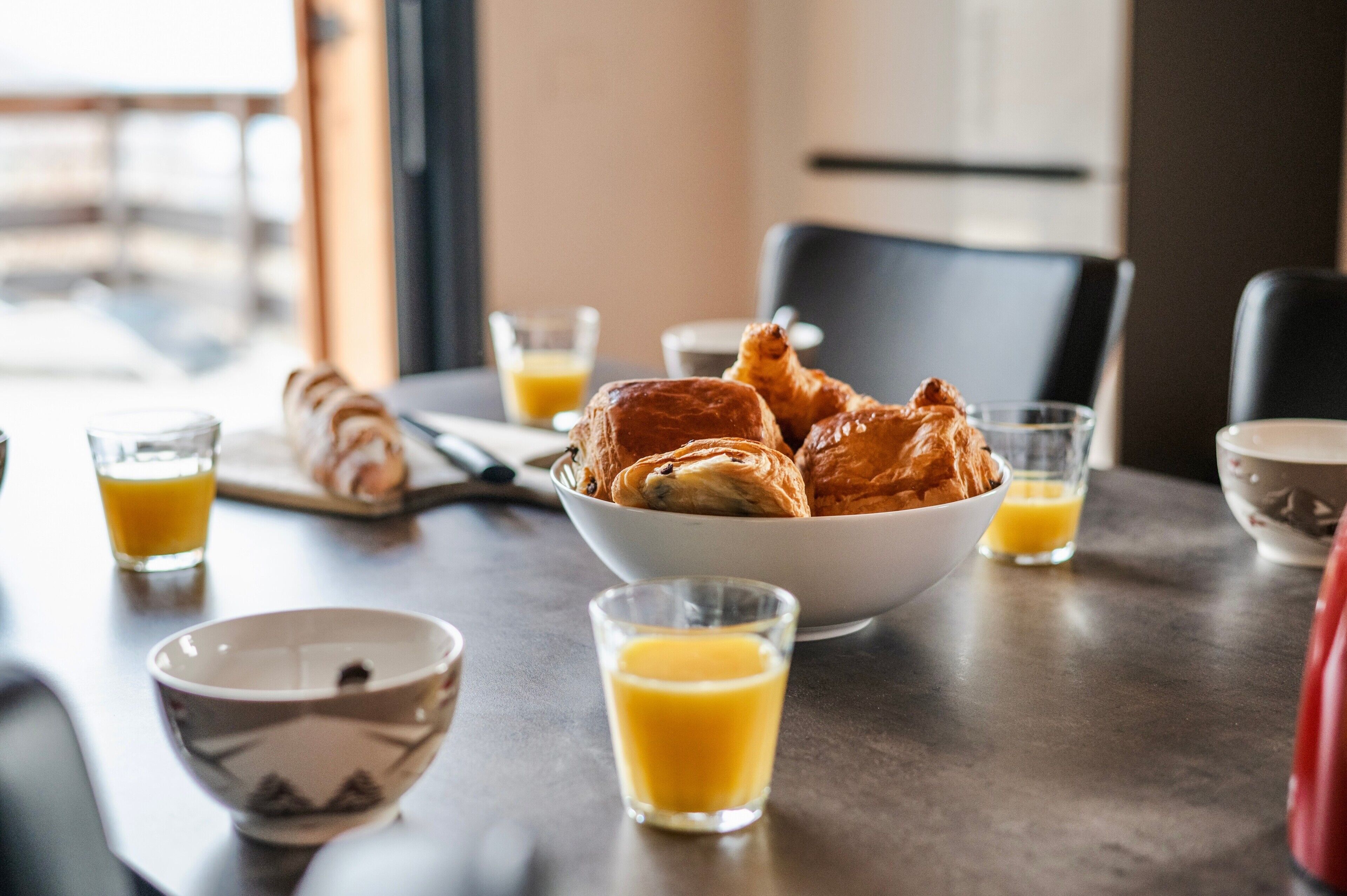 A breakfast setting with croissants, orange juice, and a bowl of pastries on a table.