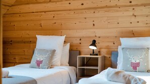 A cozy cabin room with wooden walls, two beds with matching pillows, a bedside table with a lamp, and a small shelf. - Chalet 'Au Pied De L'arcluse' with Mountain Views, Wi-Fi, and Air Conditioning (Saint-Pierre-d'Albigny)