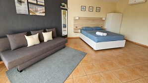 Une chambre à coucher moderne avec un canapé gris, un lit avec une literie bleue, un ventilateur de plafond et des œuvres d’art accrochées aux murs.
