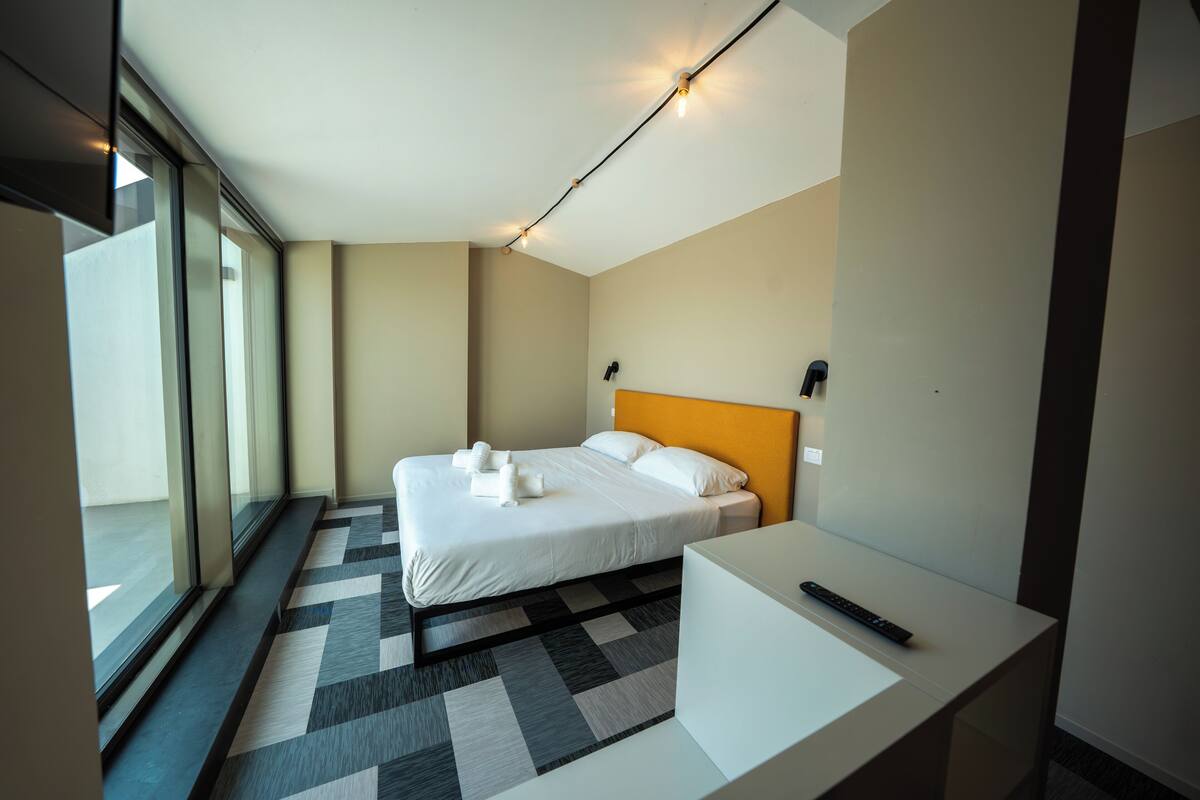 A modern hotel room with a large bed, a bedside table, and a window with a view.