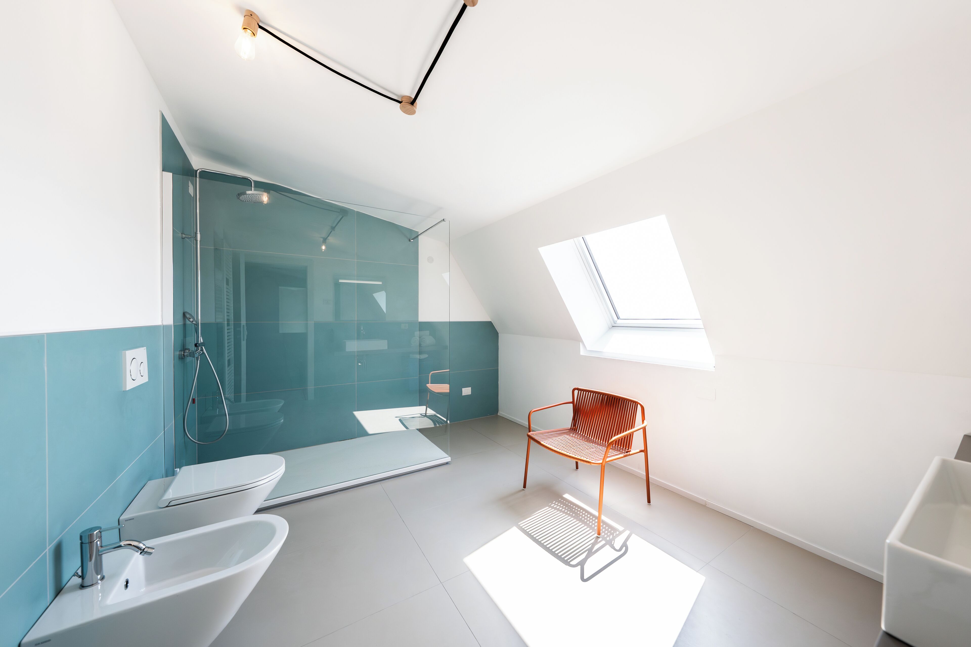 Un baño moderno con cabina de ducha de vidrio, un lavabo blanco y una silla de madera.