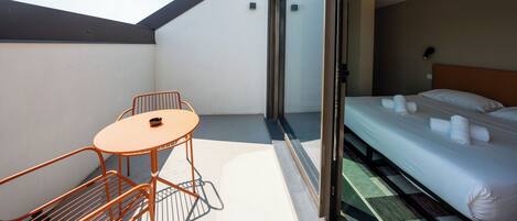 A modern hotel room with a balcony, a bed with neatly made linens, and a small round table with chairs.