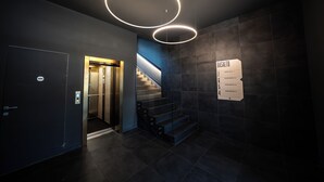 A modern elevator with a glass door, a staircase with a handrail, and a wall-mounted sign indicating apartment numbers. - BASALTO Venice Mestre Apartments (Mestre)