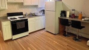 A kitchen with white cabinets, a stove, a refrigerator, a sink, and a bar area with stools. - Incredible NYC and Water Views 3 bedrooms only 15 min from NYC New Floors  (West New York)