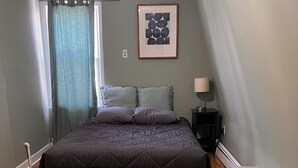 A bedroom with a large bed, a nightstand, a framed picture on the wall, and a window with curtains. - Incredible NYC and Water Views 3 bedrooms only 15 min from NYC New Floors  (West New York)