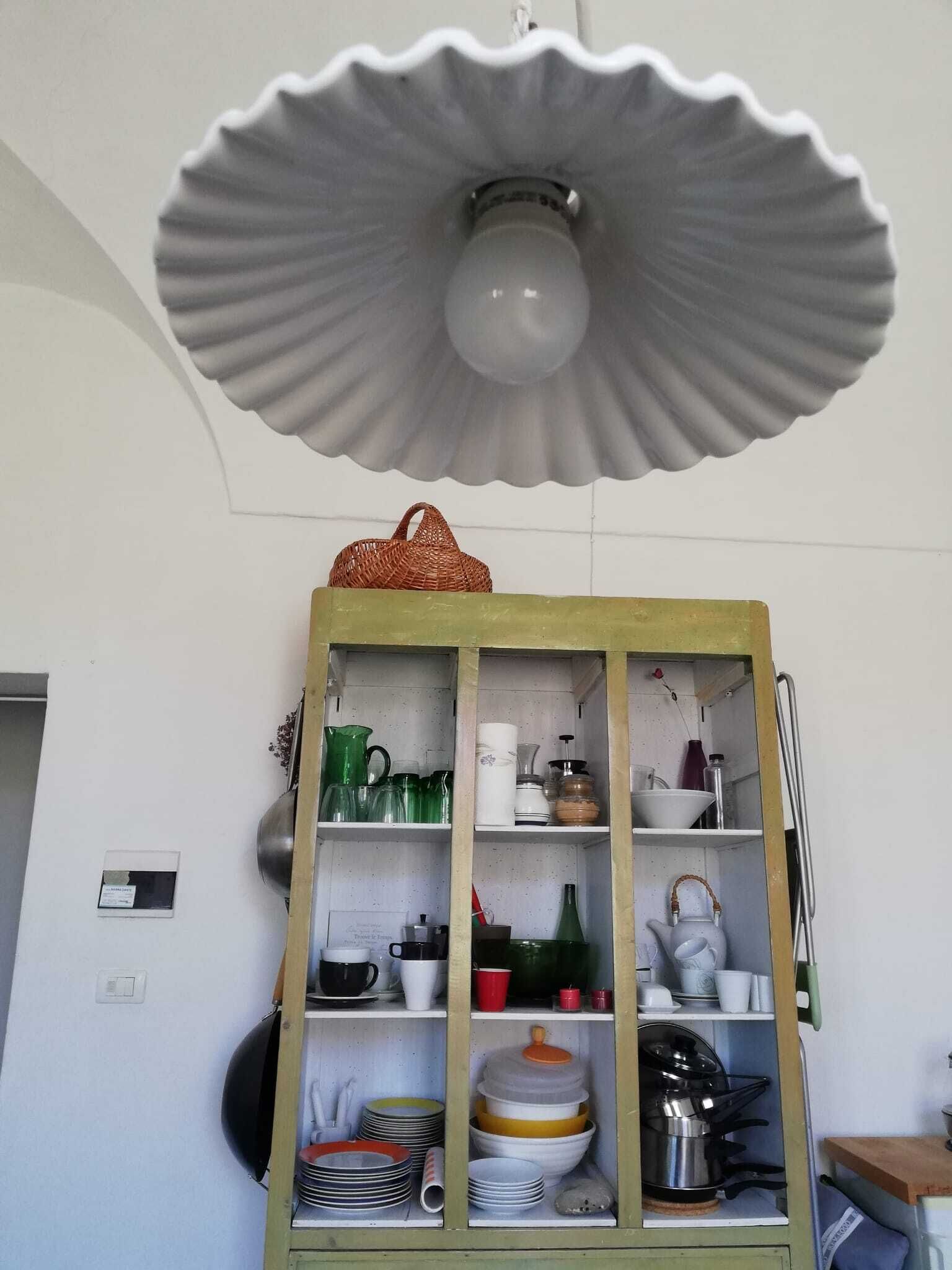 A kitchen with a large, scalloped-edged light fixture above a wooden cabinet filled with dishes and cookware.