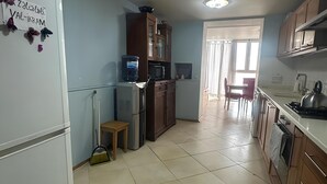 A kitchen with a refrigerator, microwave, cabinets, and a tiled floor.
