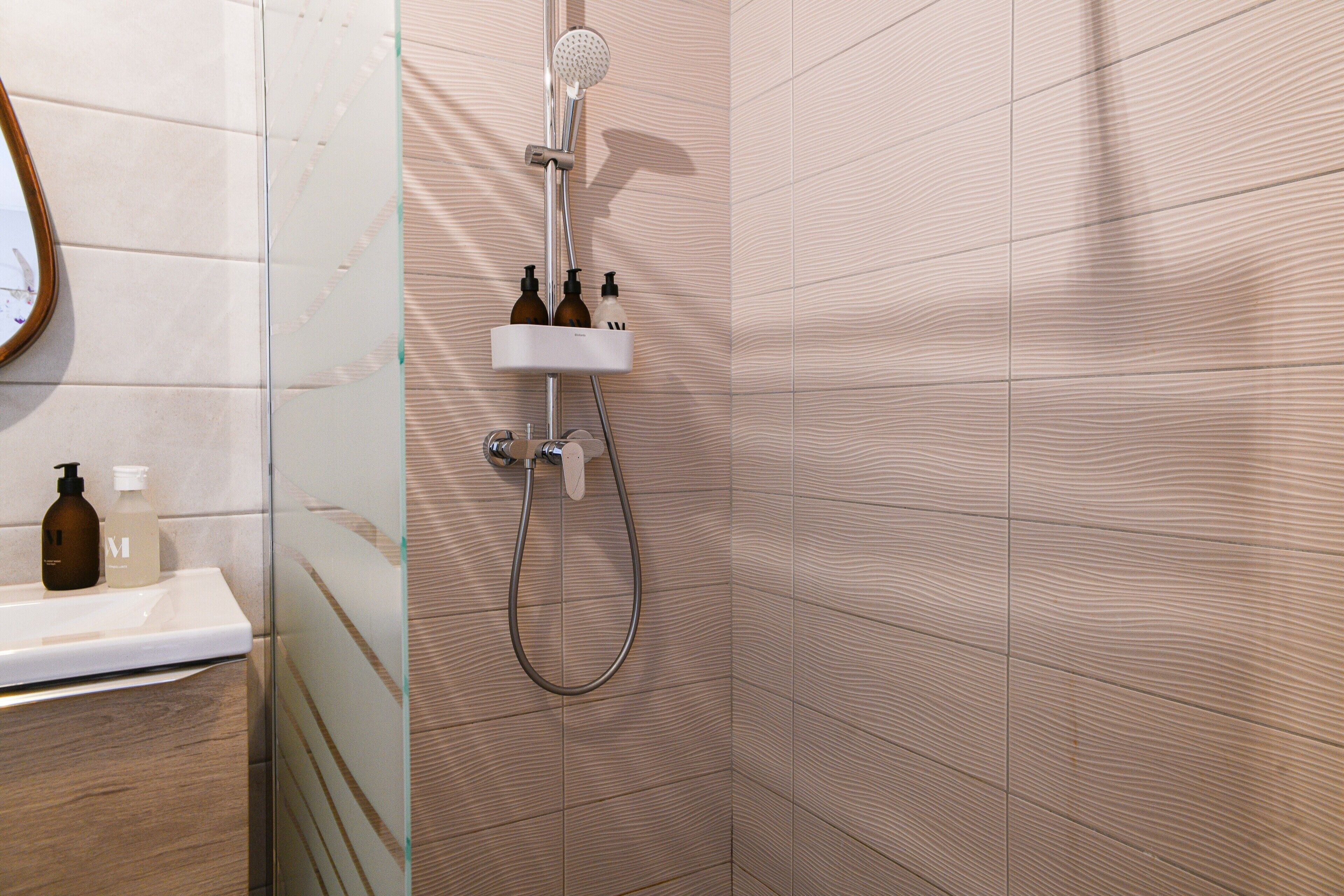 Ein Badezimmer mit Dusche, Waschbecken und zwei Shampoo-Flaschen auf der Ablagefläche.