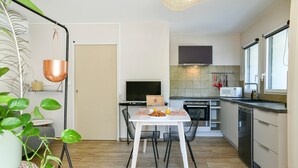 A modern kitchen with a dining table, chairs, a television, and a microwave. - Chez Flo Apartment – Cozy Studio with Mountain View and Air Conditioning (Saint-Pierre-d'Albigny)