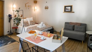 A well-lit room with a dining table set for breakfast, a sofa, a bed with a floral bedspread, and a wall-mounted picture. - Chez Flo Apartment – Cozy Studio with Mountain View and Air Conditioning (Saint-Pierre-d'Albigny)