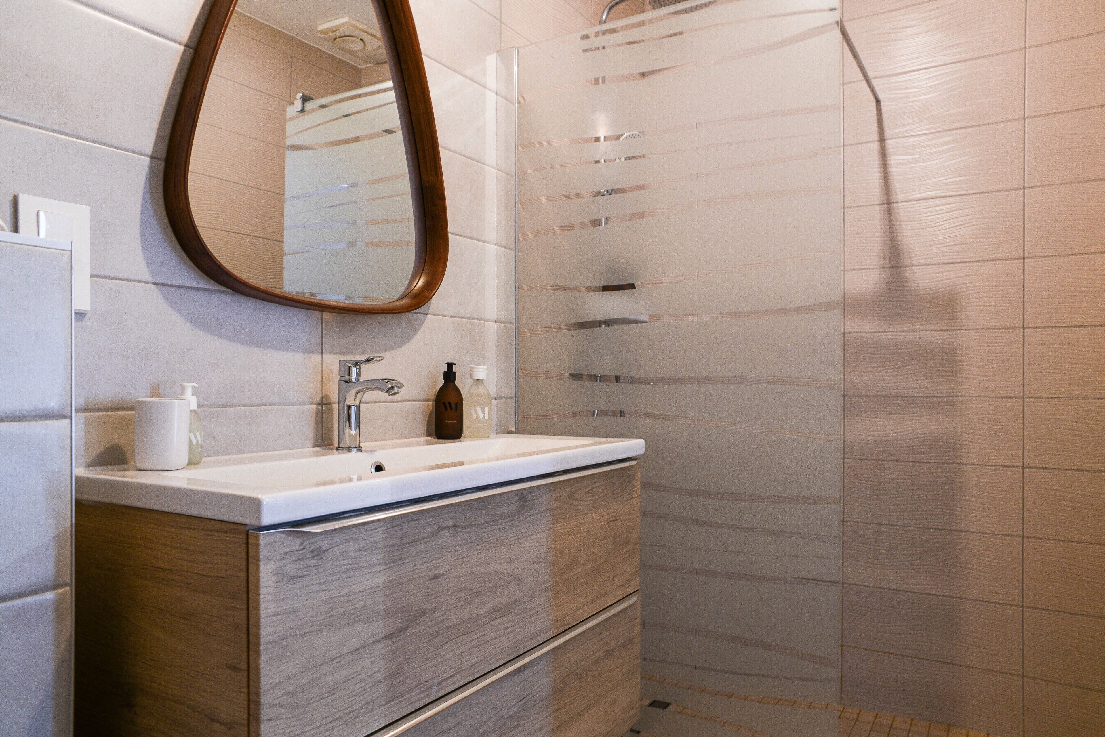 A bathroom with a wooden vanity, a mirror, a sink, and a shower enclosure.