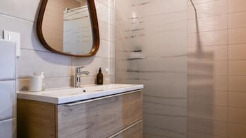Une salle de bain avec un meuble-lavabo en bois, un miroir, un lavabo et un espace douche.