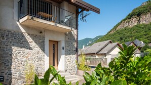 A stone building with a balcony, a wooden door, and a mountain backdrop. - Chez Flo Apartment – Cozy Studio with Mountain View and Air Conditioning (Saint-Pierre-d'Albigny)