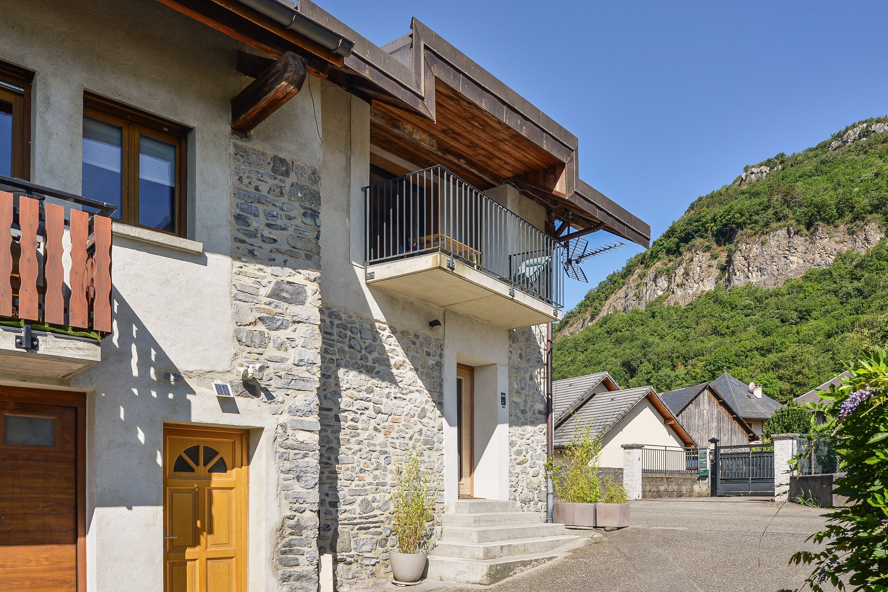 A stone building with a wooden door, a balcony, and a view of a green hillside.