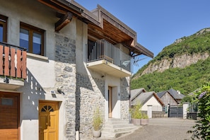 Un edificio de piedra con puerta de madera, un balcón y vista a una ladera verde.