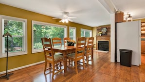 A dining area with a wooden table and chairs, a ceiling fan, and large windows with blinds.