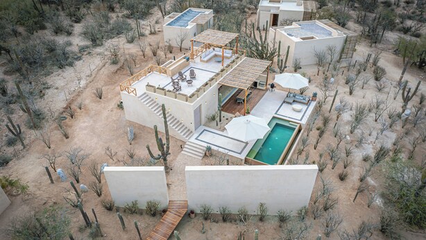Un resort en el desierto con varias construcciones, una piscina y una terraza de madera.