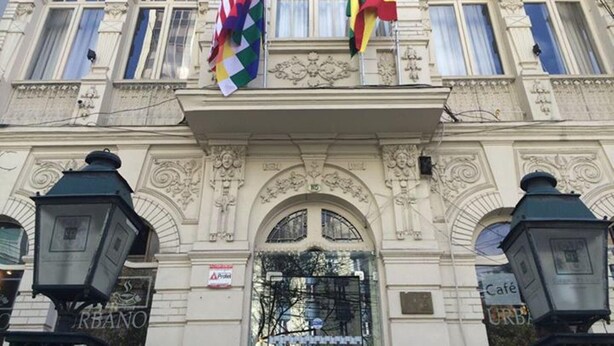 A building with ornate architectural details, including a central arched entrance and multiple windows. Flags are displayed on the facade, and there are signs indicating the presence of a café and a restaurant. - Casa Prado Suites Hotel (La Paz)
