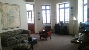 A living room with a sofa, armchair, coffee table, and a desk with a computer. There are large windows and a map on the wall. - Casa Prado Suites Hotel (La Paz)