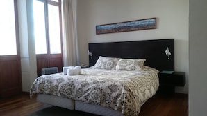 A bedroom with a large bed, a headboard, a nightstand, a lamp, a painting, and a window with curtains. - Casa Prado Suites Hotel (La Paz)