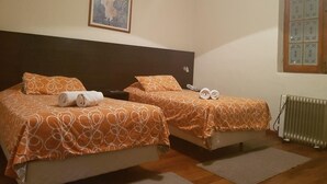 A hotel room with two beds, each with orange patterned bedding and rolled towels. There is a painting on the wall above the beds and a window with decorative tiles. - Casa Prado Suites Hotel (La Paz)