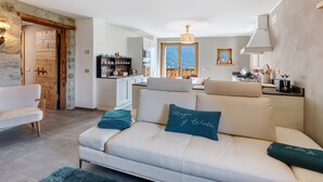 A living room with a sofa, a dining area with a table, and a kitchen in the background. - Apartment 'Marmotta' with Mountain View, Shared Garden and Wi-Fi (Oga)