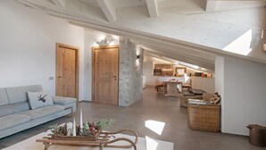 A spacious loft with a high ceiling, a cozy living area with a sofa and a wooden sled, and a kitchen in the background. - Apartment 'Scoiattolo' with Mountain View, Shared Garden and Wi-Fi (Oga)