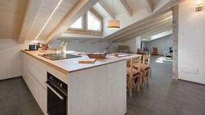 A modern kitchen with a central island, wooden ceiling beams, and a dining area with chairs. - Apartment 'Scoiattolo' with Mountain View, Shared Garden and Wi-Fi (Oga)