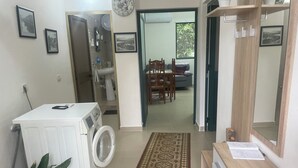 A laundry room with a washing machine, a small potted plant, and a patterned rug leading to a dining area with a table and chairs. - Hysa guest house (Shkodër)