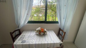 A dining area with a table set for two, a window with curtains, and a view of greenery outside. - Hysa guest house (Shkodër)
