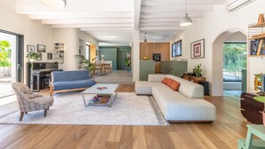 Ein geräumiges Wohnzimmer mit einer Couch, einem Sessel und einem Couchtisch, eine Küchenzeile mit modernen Geräten sowie ein Essbereich mit Stühlen.