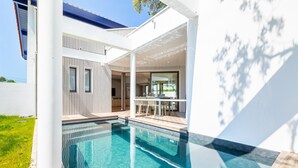 Et moderne hus med swimmingpool, patio og spiseplads.