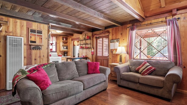 Een gezellig cabin interieur met twee banken, houten wanden, een keukenhoek en een raam met gordijnen.