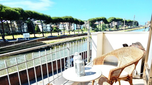 Un balcó amb mobiliari de veta, una taula i vista a un canal amb edificis al fons.