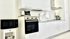 Cuina moderna amb armaris blancs, forn integrat, microones i vàter d'acer inoxidable.