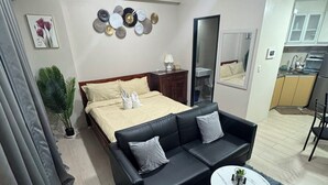 A modern bedroom with a bed, a black leather sofa, a round coffee table, and a small potted plant.