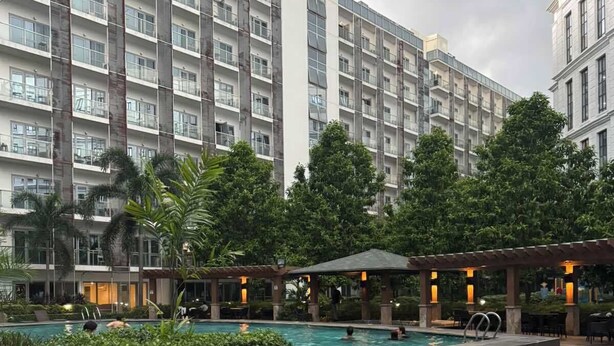 A modern hotel with a large outdoor pool, lounge areas, and lush greenery.