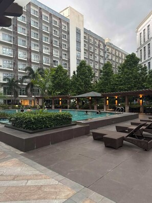 A modern hotel with a large outdoor pool, lounge areas, and lush greenery.